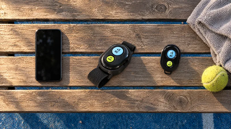 Kort bankında ekranı kapalı telefon, kayışlı ve sade Bluetooth kumanda